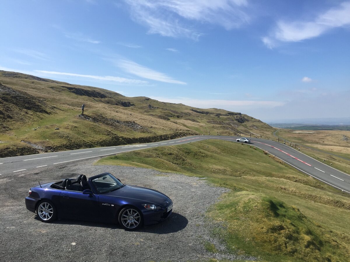 A sports car parked beside a scenic mountain road in the UK